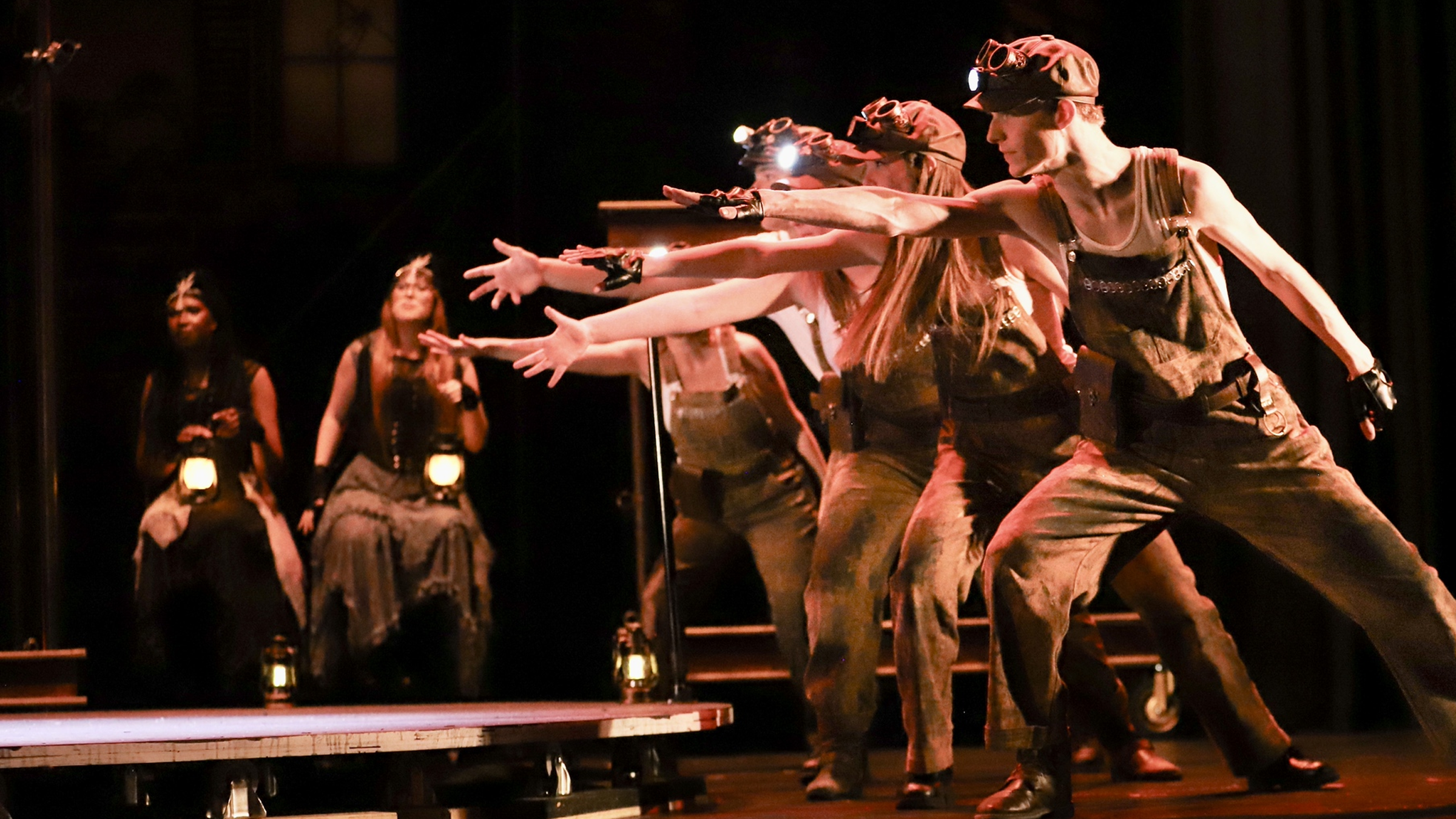 Performers with outstretched arms illuminated on a theater stage